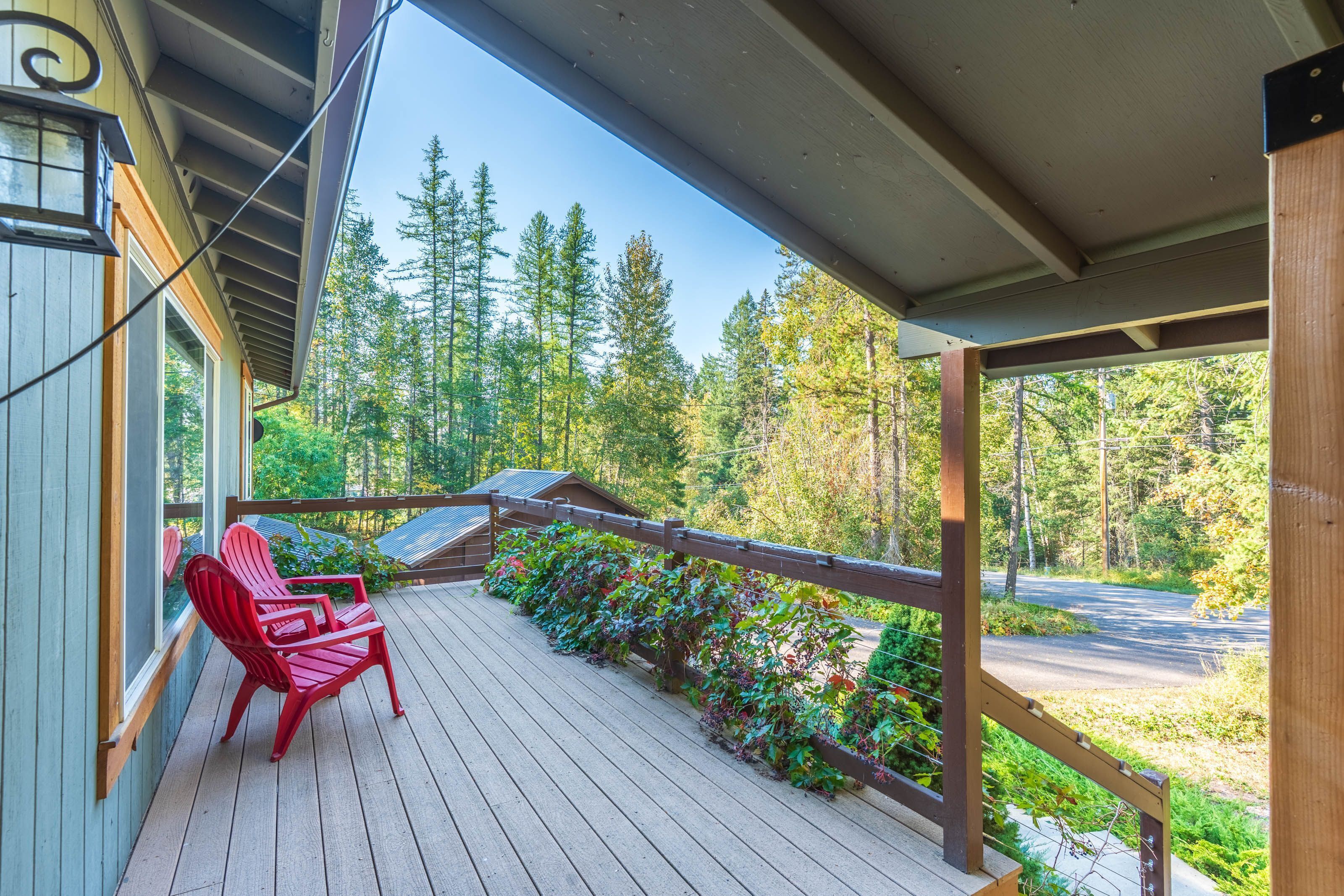 Una terraza de madera con barandilla, sillas Adirondack rojas y vistas a un bosque.