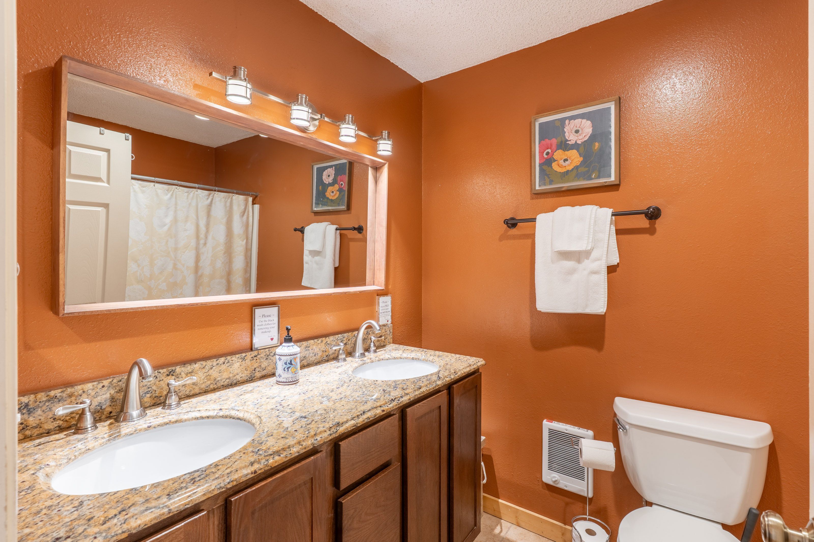 A bathroom with two sinks, a large mirror, a toilet, and a towel rack.