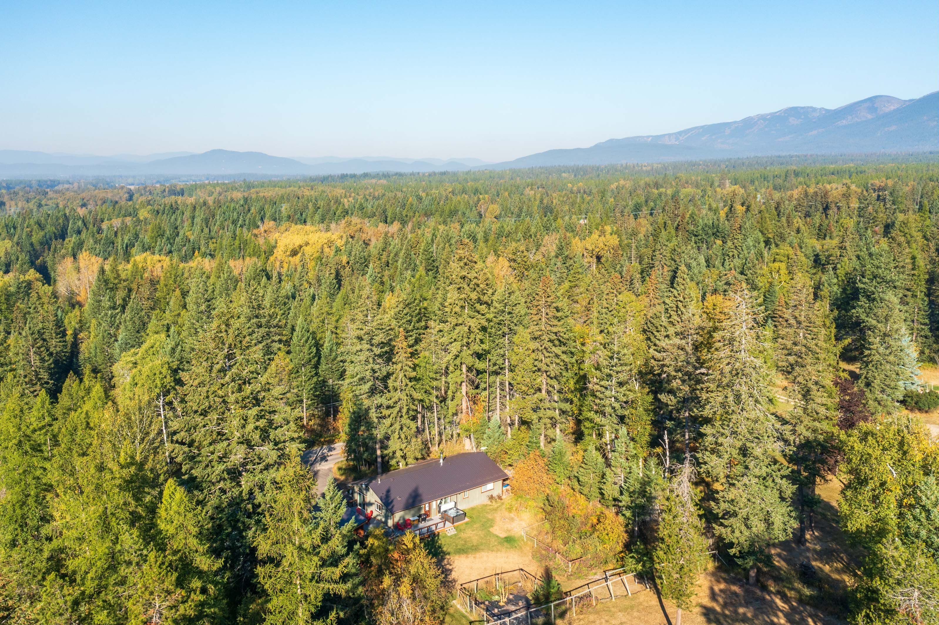 Aerial view of the home surrounded by dense forest with mountains in the background.