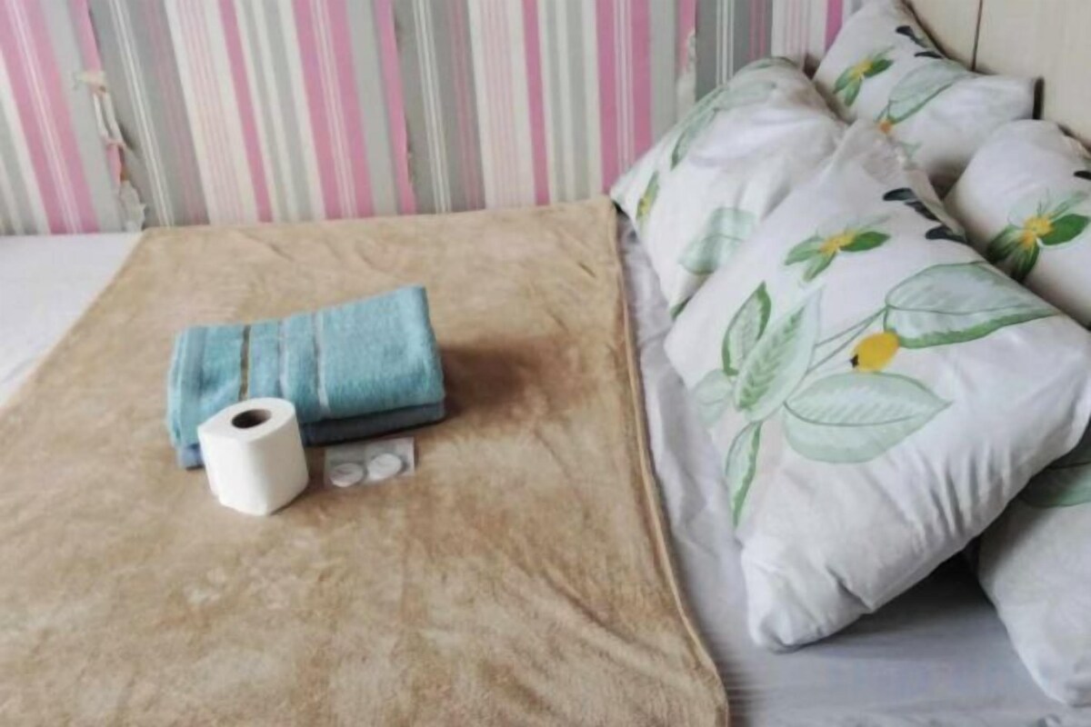 A bed with a brown cover, a blue towel, and a roll of toilet paper.