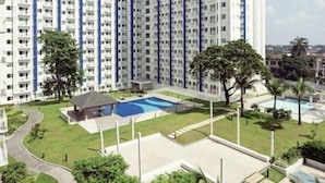 A high-rise residential building with multiple balconies, a swimming pool, and landscaped gardens.