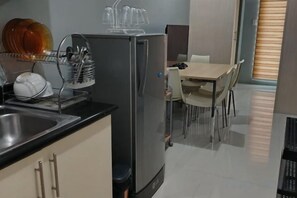 A compact kitchen with a refrigerator, sink, and a dish rack. There is a dining area with a table and chairs. - Grass Residence Tower 3 20th with balcony (Quezon City)