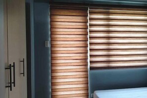 Una habitación con cama, armario y ventana con persianas horizontales.
