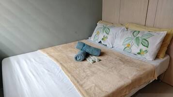 A neatly made bed with a beige bedspread, two pillows with floral patterns, and a rolled towel on the bed.
