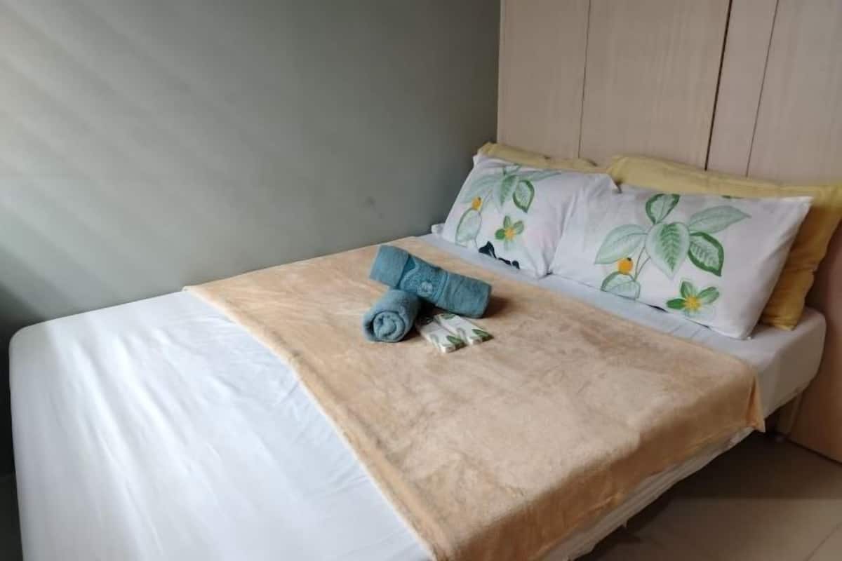 Una cama bien hecha con una colcha color beige, dos almohadas con estampado floral y una toalla azul.