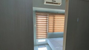 A narrow room with a bed, a window with blinds, and an air conditioning unit. - Grass Residence Tower 3 20th with balcony (Quezon City)