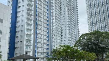 A high-rise residential building with multiple balconies, surrounded by greenery and a small pavilion.