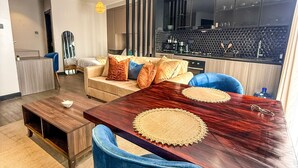 A modern living room with a dark wooden dining table, blue chairs, and a sofa with patterned cushions. - Luxury Studio Apartment in Nairobi (Nairobi)