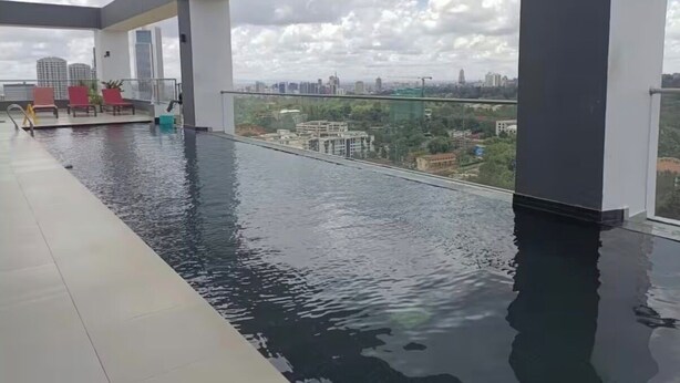 A rooftop infinity pool with a city view, red lounge chairs, and a glass railing. - Luxury Studio Apartment in Nairobi (Nairobi)
