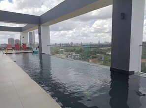 A rooftop infinity pool with a city view, red lounge chairs, and a glass railing. - Luxury Studio Apartment in Nairobi (Nairobi)