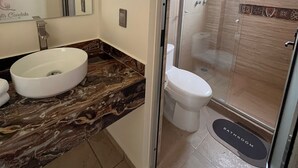 A bathroom with a marble countertop, a white sink, a toilet, and a glass-enclosed shower. - Quinta Candela Hotel (Chignahuapan)