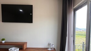 A modern room with a wooden desk, a black chair, a television mounted on the wall, and a view of a green landscape through a large window. - Quinta Candela Hotel (Chignahuapan)