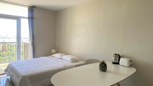 A modern hotel room with a bed, a round dining table, a chair, a small potted plant, a kettle, and a toaster. - Cheap Accommodation - Saekyung Apartment (Lapu-Lapu)