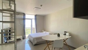 A modern hotel room with a bed, a dining table with chairs, a kitchenette, and a balcony with a view. - Cheap Accommodation - Saekyung Apartment (Lapu-Lapu)