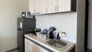A compact kitchen with light wood cabinets, a black refrigerator, a microwave, and a sink. - Cheap Accommodation - Saekyung Apartment (Lapu-Lapu)