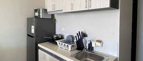 A compact kitchen with light wood cabinets, a black refrigerator, a microwave, and a sink.