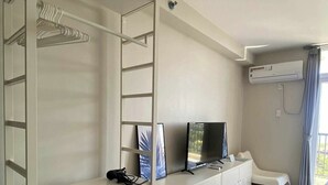 A hotel room with a white wardrobe, a TV, a desk with a chair, and an air conditioning unit. - Cheap Accommodation - Saekyung Apartment (Lapu-Lapu)