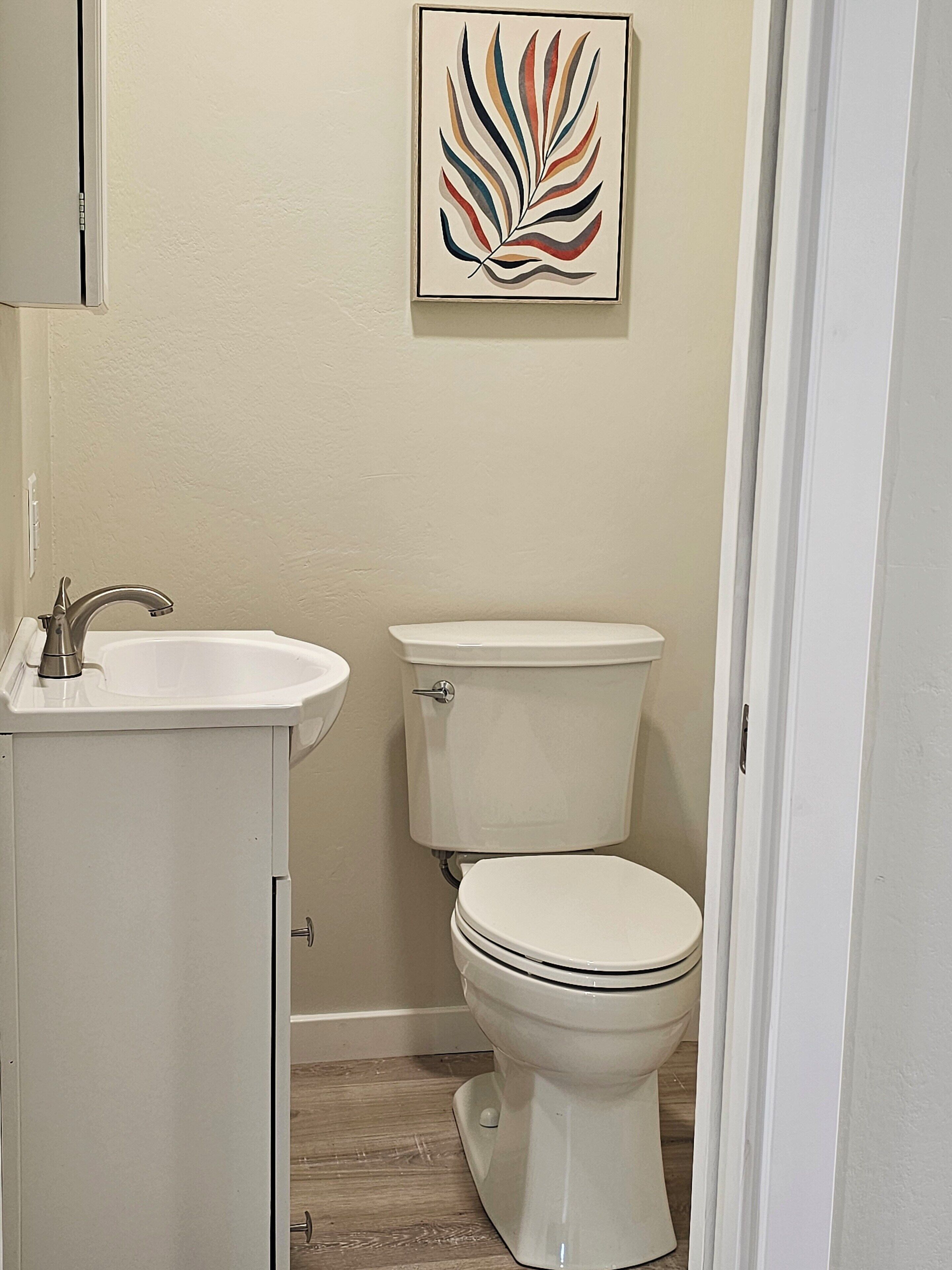 A bathroom with a white sink, a toilet, and a framed artwork on the wall.