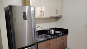 Una cocina compacta con un refrigerador de acero inoxidable, armarios de madera, un lavamanos y un cubo de basura.