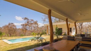 A covered outdoor area with a pool, seating, and a view of trees.