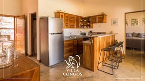 A kitchen with wooden cabinets, a stainless steel refrigerator, and a bar area with stools.