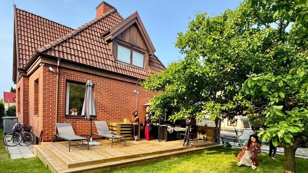 Una casa a due piani in mattoni con tetto in tegole, un patio in legno e un prato.