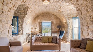 A cozy living room with stone walls, a large window, and a sofa with cushions. - Red Oak House With Garden & Terrace in Assia, Batroun (Bchaaleh)