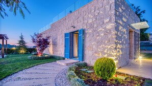 A modern stone building with a glass facade, a stone pathway, and a well-maintained garden with various plants and a small tree. - Red Oak House With Garden & Terrace in Assia, Batroun (Bchaaleh)