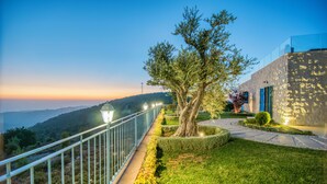 A pathway leading to a building with a stone facade, a tree, and a railing overlooking a hilly landscape. - Red Oak House With Garden & Terrace in Assia, Batroun (Bchaaleh)