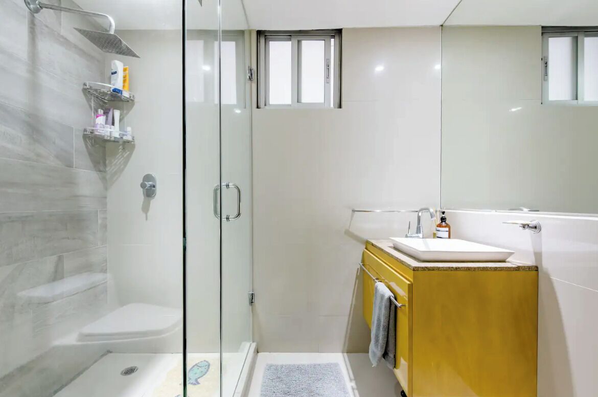 Une salle de bain moderne avec une douche à l’italienne en verre, un lavabo blanc et un meuble-lavabo jaune.