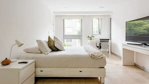 Ein modernes Schlafzimmer mit Bett, Nachttisch, Fernseher und Blick ins Freie.