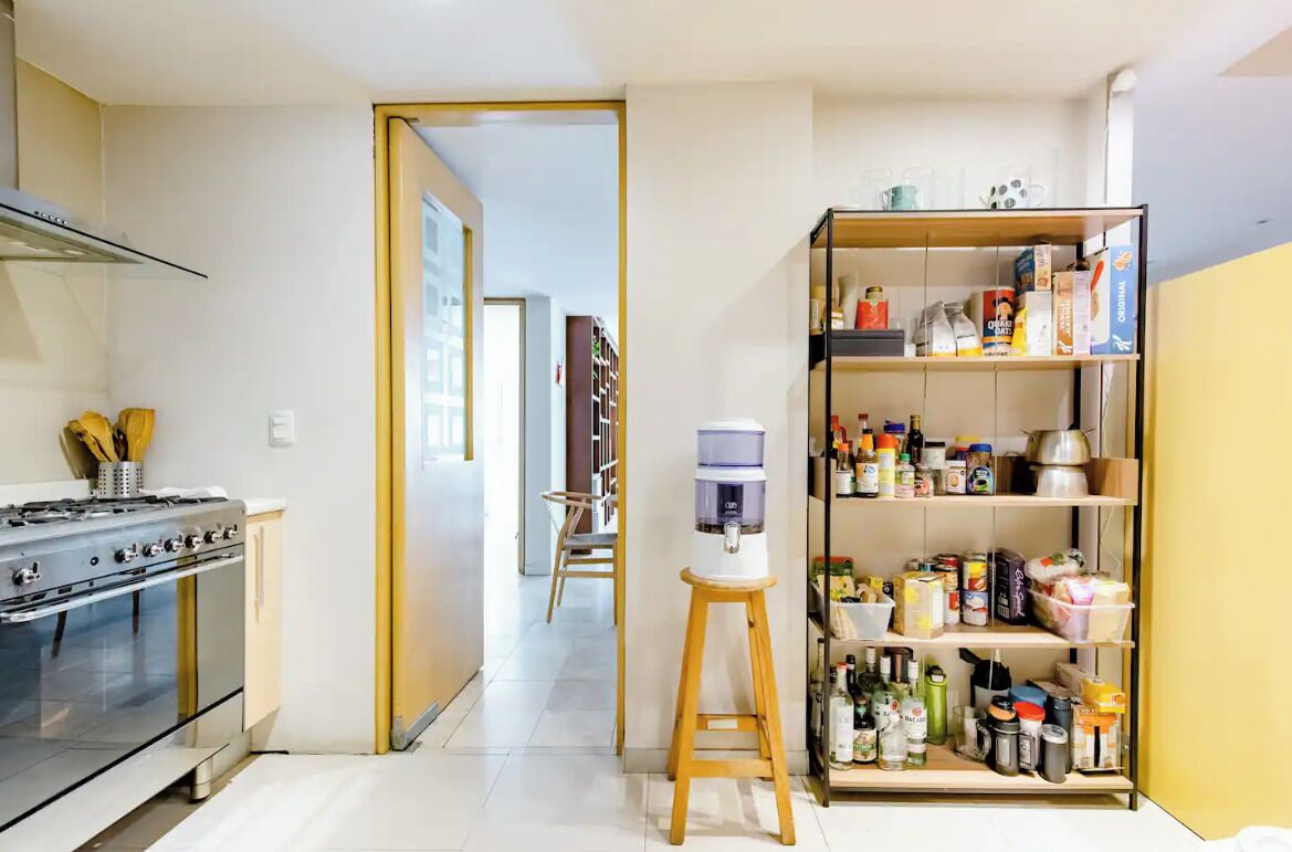 A kitchen with a stove, a water dispenser, and a pantry stocked with food items.