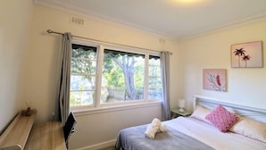 A bedroom with a bed, a desk, a window with curtains, and wall art.