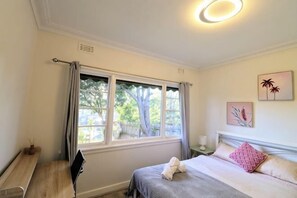 A bedroom with a bed, a desk, a window with curtains, and wall art. - Humble Abode near Station, Costco, Eastland (Heathmont)