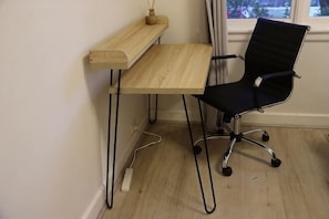 A workspace with a wooden desk, a black office chair, and a power outlet on the floor. - Humble Abode near Station, Costco, Eastland (Heathmont)