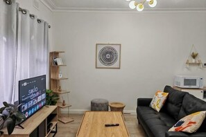 A living room with a TV, wooden coffee table, black sofa, and a bookshelf. - Humble Abode near Station, Costco, Eastland (Heathmont)