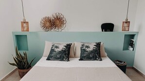 Un lit avec deux oreillers, une petite plante et une étagère fixée au mur sur laquelle est posée une image.
