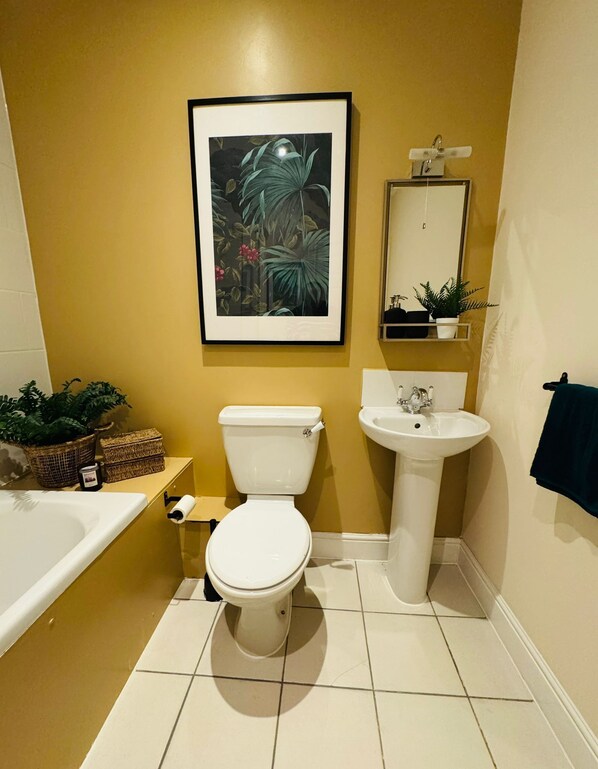 A bathroom with a toilet, sink, and bathtub. There is a framed picture on the wall and a potted plant on the counter.