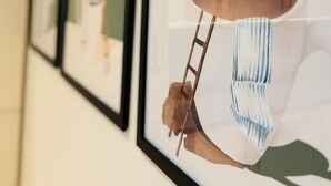 En vägg med inramade konstverk som föreställer en person som håller i en stege och en fågel.
