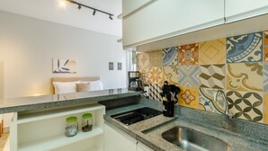 Una cocina moderna con estufa integrada, cafetera y fregadero. Hay dos frascos en un estante debajo de la encimera.