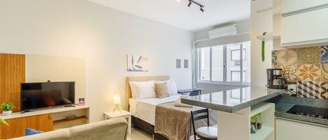 A modern hotel room with a bed, a TV, a desk, and a kitchenette.