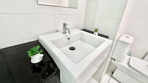 Un baño con lavamanos blanco, encimera negra y una pequeña planta en maceta.
