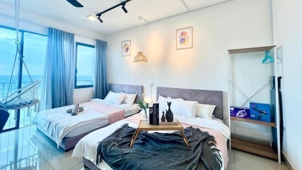 Habitación de hotel con dos camas, ventilador de techo, vista al mar y balcón con una silla colgante.