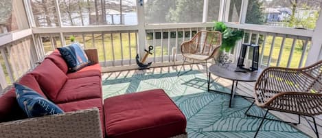 A covered porch with a cushioned seating area, a small table, and chairs.