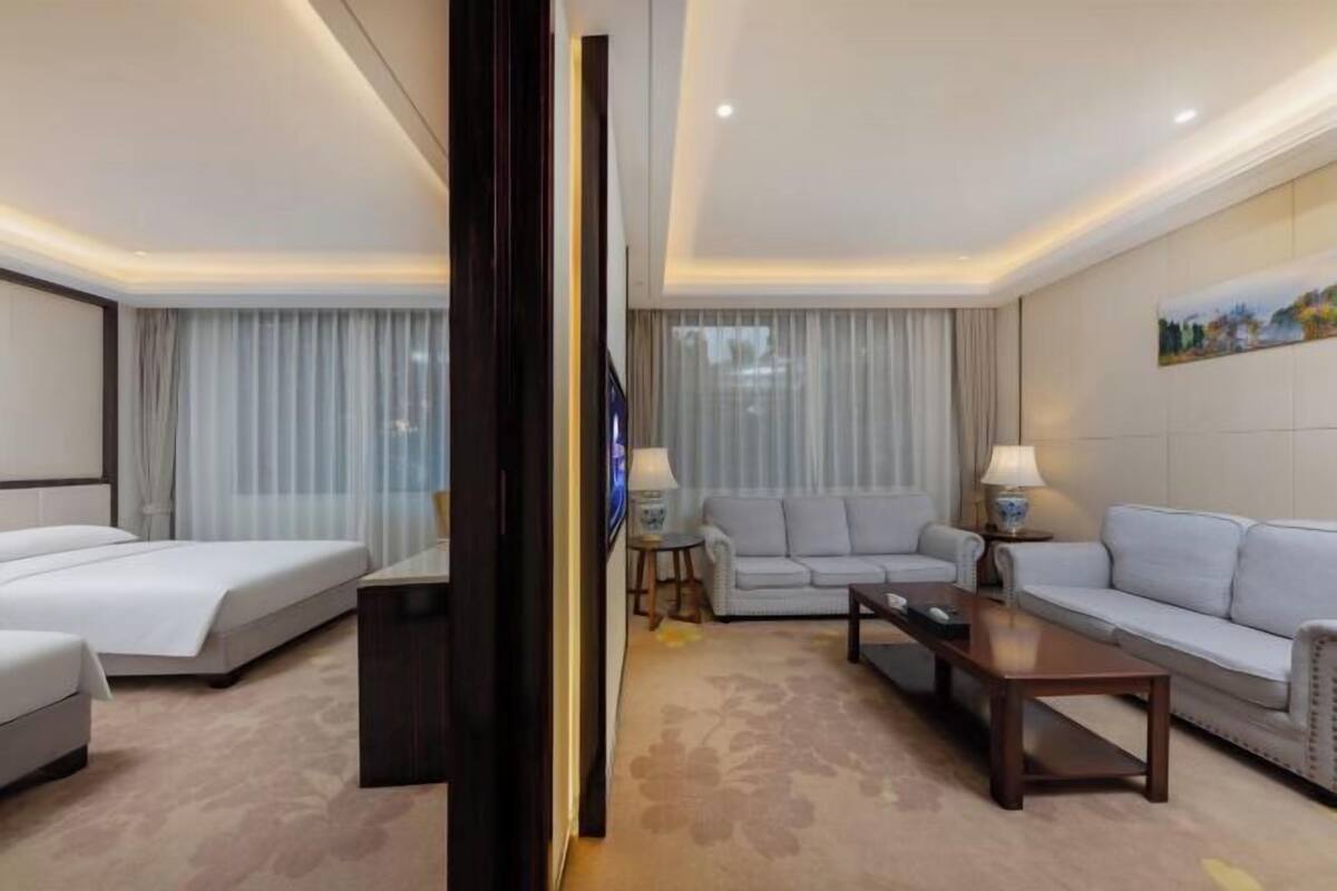 A hotel room with a bed, two sofas, a TV, and a coffee table.