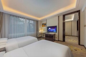 Ein Hotelzimmer mit zwei Betten, einem Schreibtisch, einem Fernseher und einem großen Fenster mit Vorhängen.