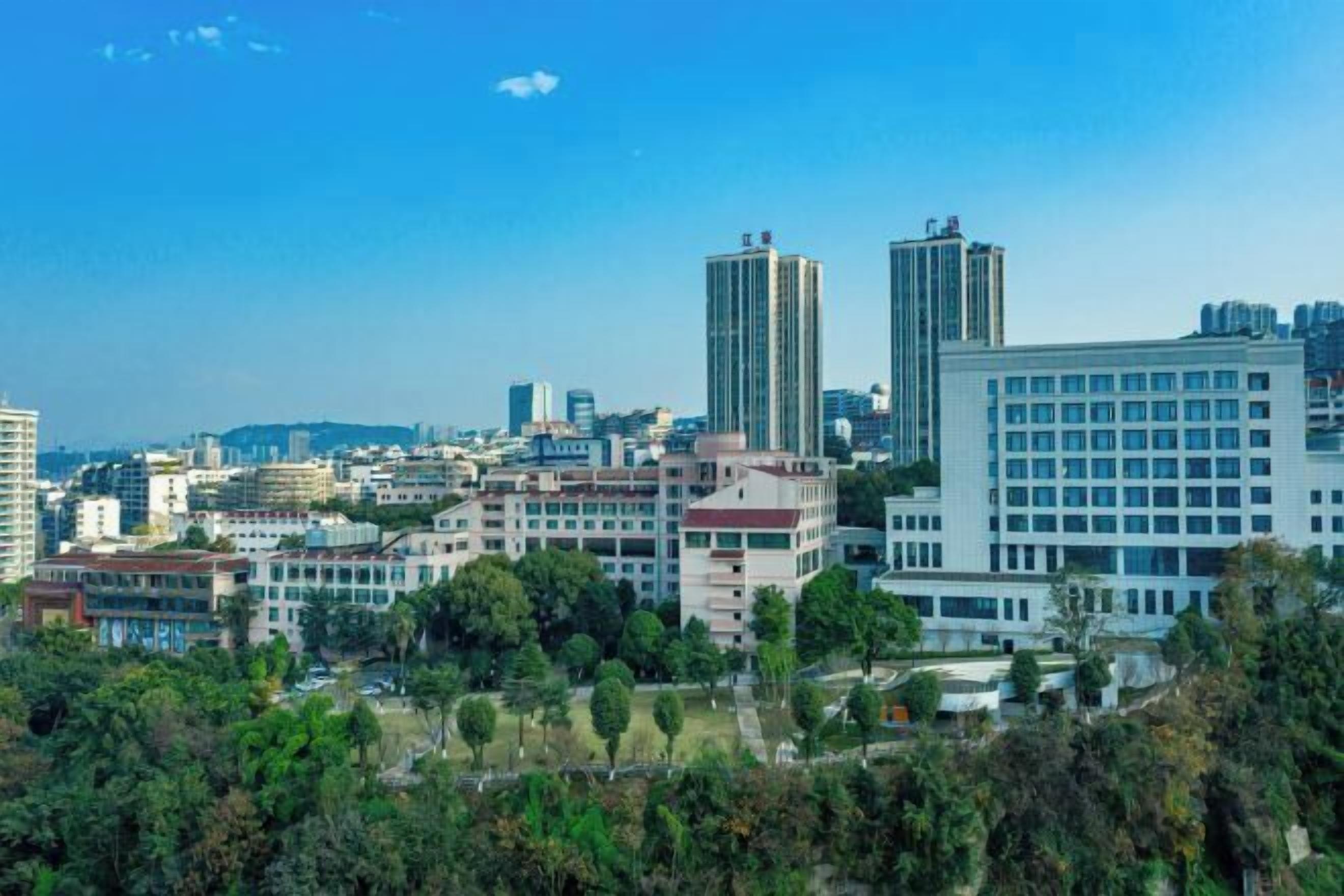 A cityscape with modern buildings, a large white building with a grid of windows, and surrounding greenery.