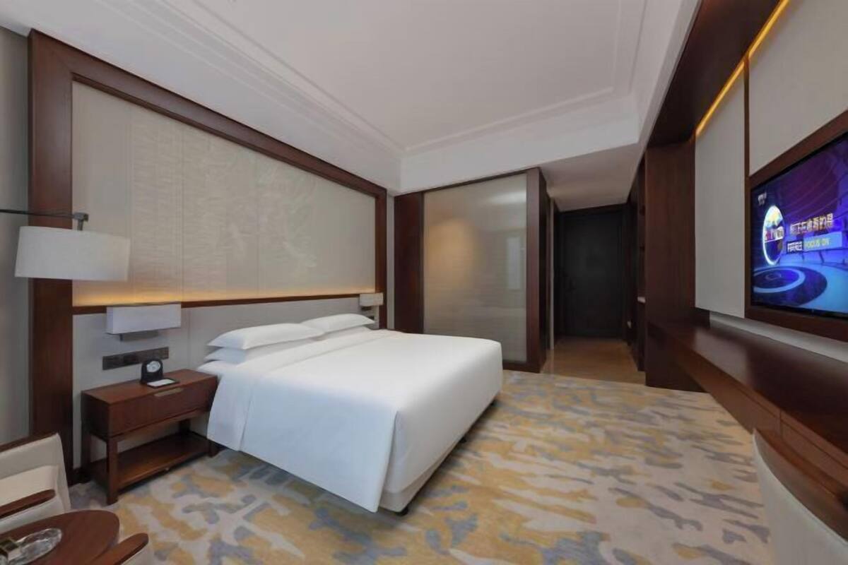 A hotel room with a bed, a TV, a nightstand, and a patterned carpet.