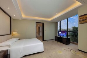 Ein Hotelzimmer mit Bett, Fernseher und großem Fenster mit Blick auf die Stadt.