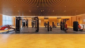 Una palestra con diverse attrezzature per esercizi, pannelli di legno a soffitto e un'ampia finestra a sinistra.